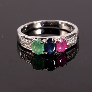 May include: A silver ring with three oval-shaped gemstones. The gemstones are green, blue, and pink. The ring is set with small diamonds.