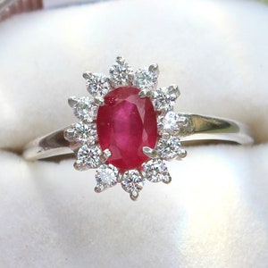 May include: A silver ring with a large oval ruby surrounded by a halo of smaller diamonds.