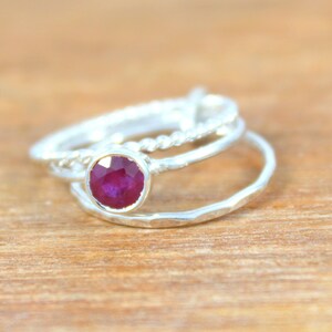 Peut inclure: Trois bagues en argent avec une pierre pr&eacute;cieuse rouge au centre. Les bagues sont empil&eacute;es les unes sur les autres. La bague du bas est textur&eacute;e, la bague du milieu est unie et la bague du haut est torsad&eacute;e.
