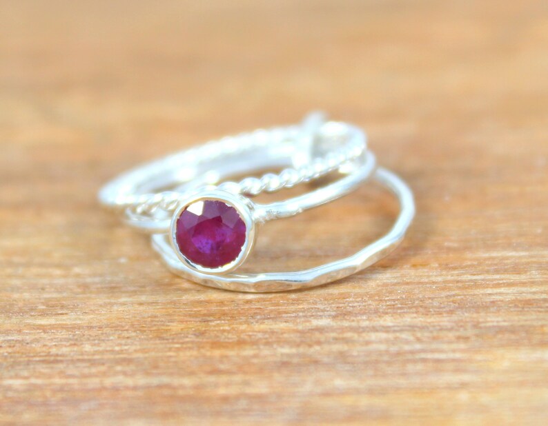 Peut inclure: Trois bagues en argent avec une pierre pr&eacute;cieuse rouge au centre. Les bagues sont empil&eacute;es les unes sur les autres. La bague du bas est textur&eacute;e, la bague du milieu est unie et la bague du haut est torsad&eacute;e.