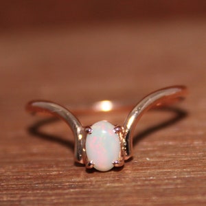 May include: A delicate rose gold ring with a white opal gemstone set in a curved band.