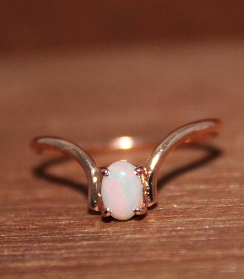 May include: A delicate rose gold ring with a white opal gemstone set in a curved band.