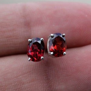 May include: A pair of silver stud earrings with oval-shaped red gemstones.