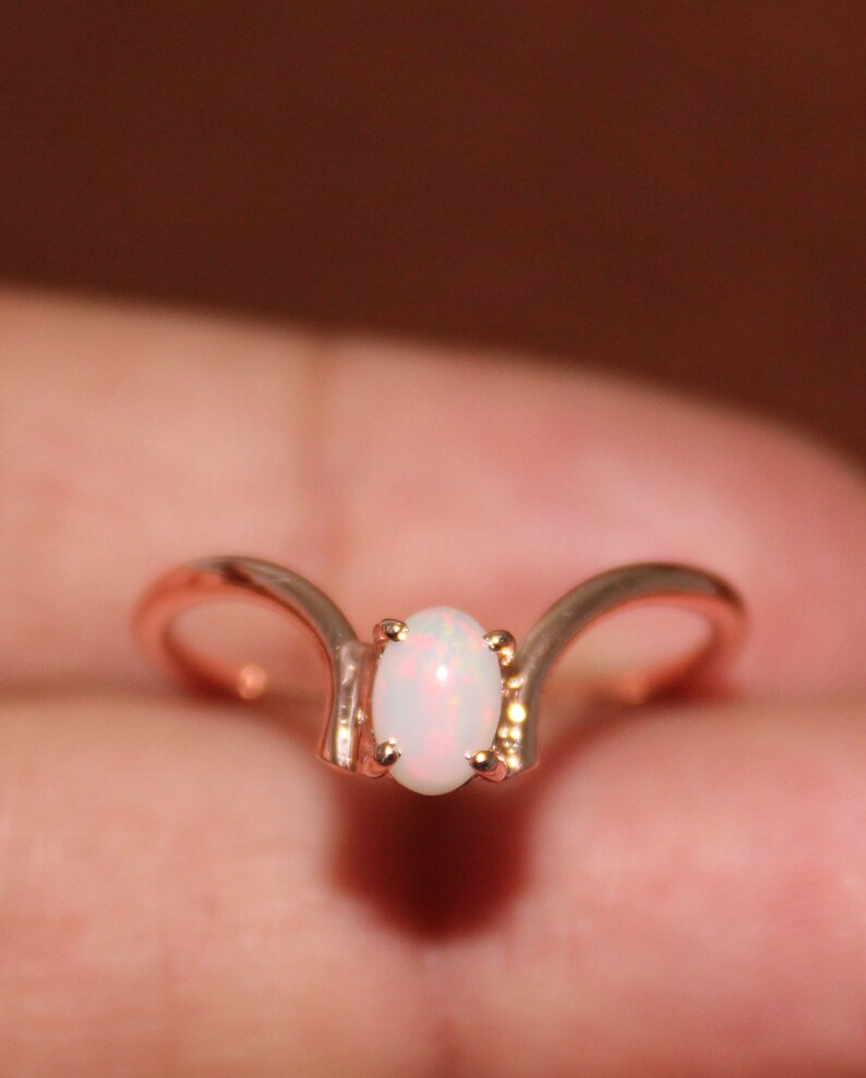 May include: A delicate rose gold ring with a white opal gemstone set in a unique curved design.
