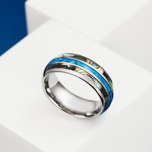 May include: A silver ring with a blue and iridescent inlay. The ring has a polished finish and a wide band.