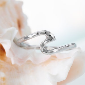 May include: A silver wave ring with a hammered texture. The ring is on a white seashell background.