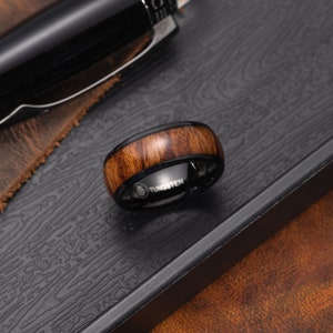 May include: A black tungsten ring with a brown wood inlay. The ring has the word "Tungsten" engraved on the band.