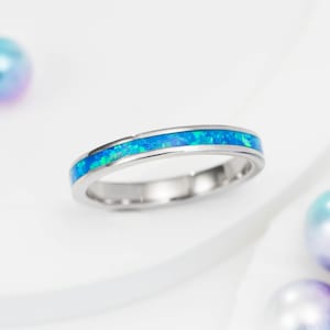 May include: A thin silver band ring with a blue opal inlay.