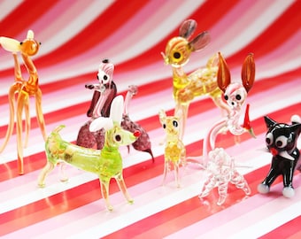 May include: A collection of colourful glass animal figurines, including a deer, a cat, a bird, and a dog. The figurines are arranged on a red and white striped background.