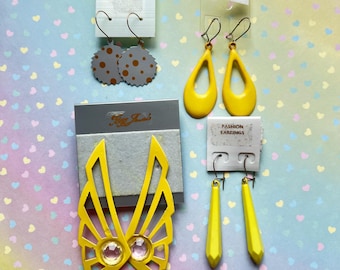 May include: A selection of vintage fashion earrings. The image shows several pairs, including gray polka dot, yellow teardrop, wing-shaped with gems, and geometric designs. Each pair is presented on its original card, showcasing the earrings' unique styles.