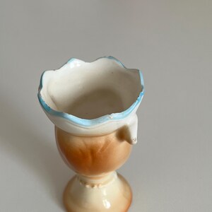 May include: A small, ceramic vase with a scalloped rim and a blue and white glaze. The vase has a brown and white glaze on the bottom half and a pedestal base.