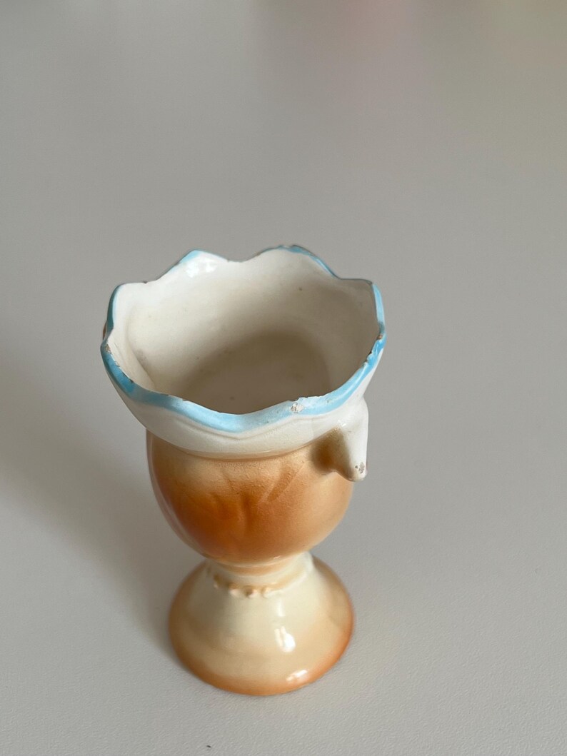 May include: A small, ceramic vase with a scalloped rim and a blue and white glaze. The vase has a brown and white glaze on the bottom half and a pedestal base.