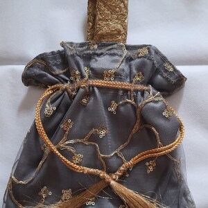 May include: A gray drawstring bag with gold embroidery and tassels. The bag has a gold handle and gold bells on the bottom.