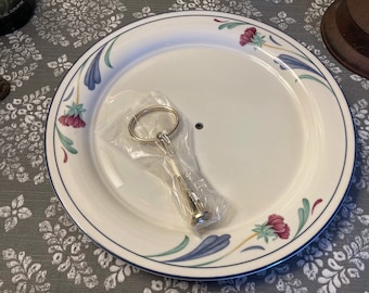 May include: A white ceramic cake stand with a blue and green floral design. The stand has a removable center piece for serving.