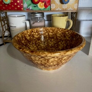 May include: A large, brown and yellow speckled ceramic bowl. The bowl has a mottled glaze and a slightly rounded shape.