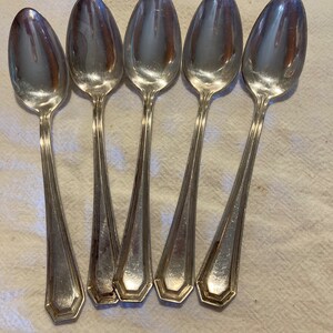 May include: Set of five silver teaspoons with ornate handles. The spoons are arranged in a row, with the handles pointing towards the viewer.