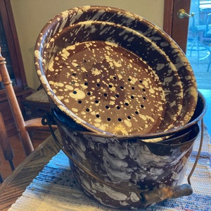 May include: A set of three vintage brown and white speckled metal colanders with a handle. The colanders are nested together and have a white speckled pattern.