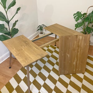 May include: A wooden table with a light brown finish and a diamond patterned rug underneath. The table has two leaves that can be extended to make it longer.