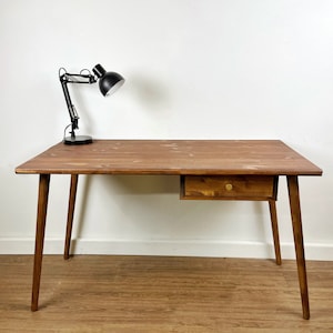 May include: A dark brown wooden desk with a single drawer and tapered legs. A black desk lamp is on the desk.