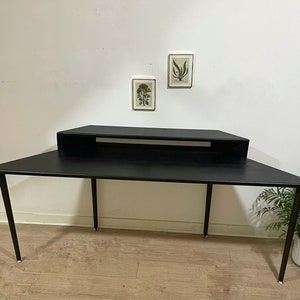 May include: A black desk with a shelf underneath. The desk has a simple design with straight lines and a rectangular shape. The desk is made of metal and has a black finish.