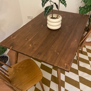 May include: A dark brown wooden dining table with a light brown wooden chair. The table has a simple design with four legs and a rectangular top. The chair has a slatted back and a solid seat. The table and chair are on a brown and white checkered rug.
