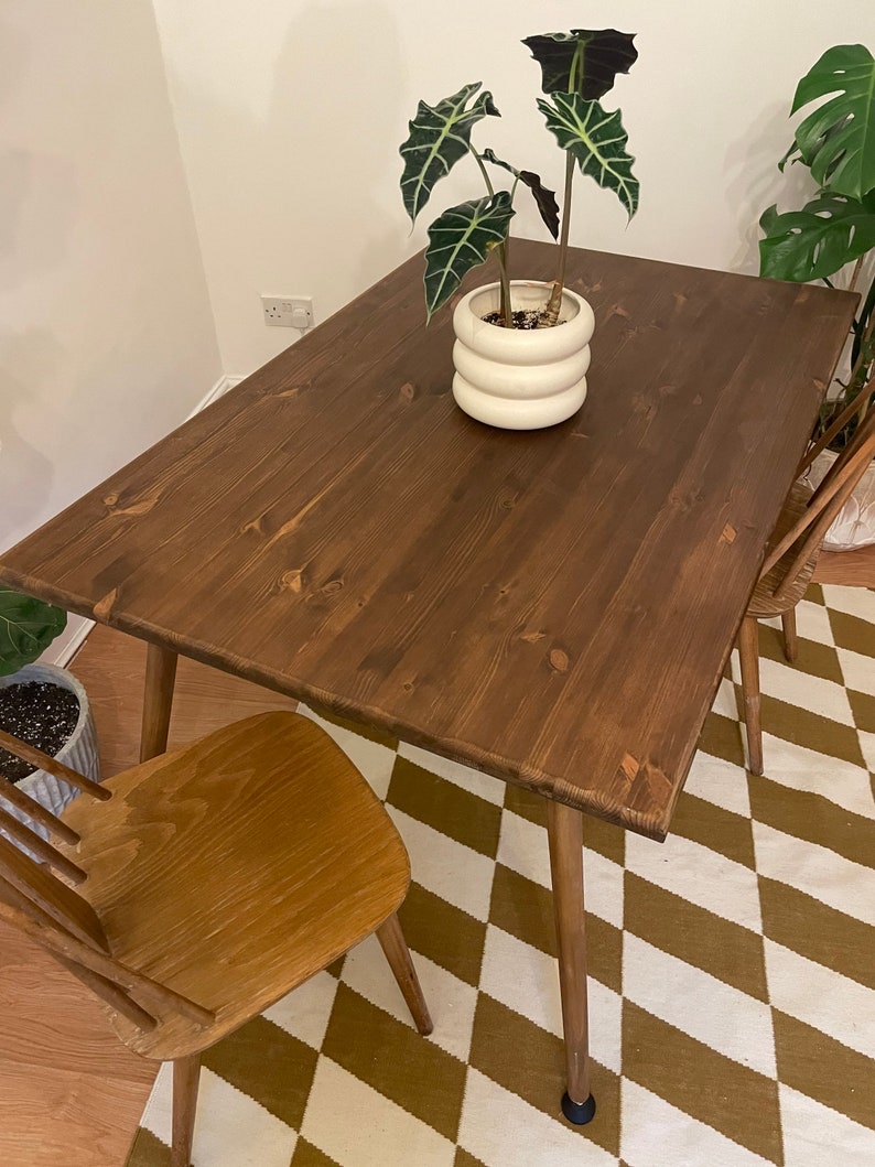 May include: A dark brown wooden dining table with a light brown wooden chair. The table has a simple design with four legs and a rectangular top. The chair has a slatted back and a solid seat. The table and chair are on a brown and white checkered rug.