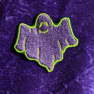 Könnte beinhalten: Lilafarbener gestickter Geister-Patch mit grünem Umriss. Der Geist hat ein lächelndes Gesicht.