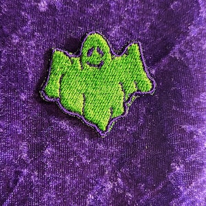May include: Green embroidered ghost patch with a smiling face. The patch is on a purple background.