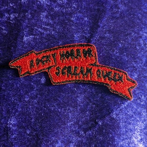 Peut inclure: Patch brodé rouge avec des points noirs. Le patch représente une bannière avec le texte "Party Hard" et "Scream Often".