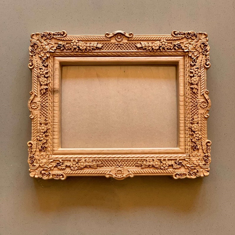 May include: A wooden picture frame with ornate carvings and a light brown finish.