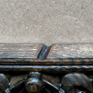 May include: Close-up of a dark wood picture frame with a decorative carved edge. The frame has a black stain and a natural wood grain pattern.