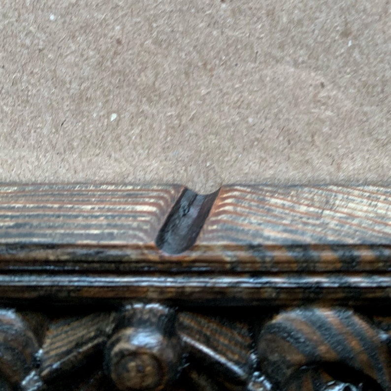 May include: Close-up of a dark wood picture frame with a decorative carved edge. The frame has a black stain and a natural wood grain pattern.