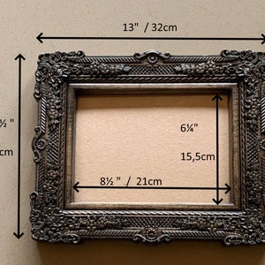 May include: A dark brown ornate picture frame with a 13 inch by 8 1/2 inch opening. The frame is 10 1/2 inches tall and 13 inches wide. The frame has a decorative design with floral motifs.