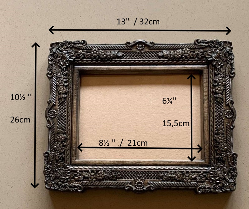 May include: A dark brown ornate picture frame with a 13 inch by 8 1/2 inch opening. The frame is 10 1/2 inches tall and 13 inches wide. The frame has a decorative design with floral motifs.