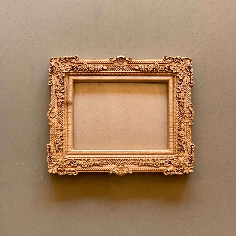 May include: A wooden picture frame with an ornate, carved design. The frame is a light brown color and has a rectangular shape.
