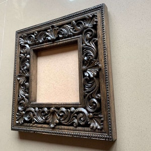 May include: A dark brown wooden picture frame with intricate carvings around the edges. The frame is empty and ready to display a photo or artwork.