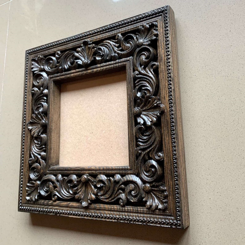 May include: A dark brown wooden picture frame with intricate carvings around the edges. The frame is empty and ready to display a photo or artwork.