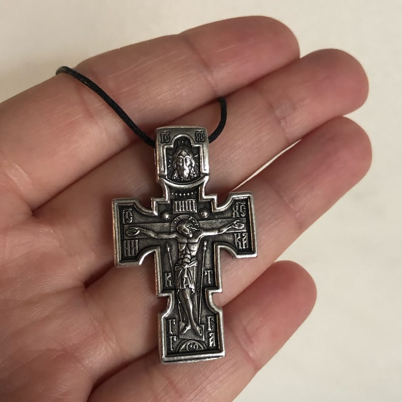 K&ouml;nnte beinhalten: Ein silberfarbener Kreuzanh&auml;nger mit filigranen Details und einer Darstellung von Jesus Christus am Kreuz. Das Kreuz befindet sich an einer schwarzen Schnur.