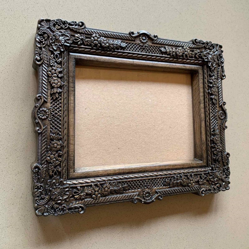 May include: A dark brown ornate picture frame with a carved design. The frame has a rectangular shape and a raised edge.