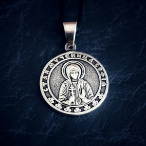 May include: Silver pendant with a religious icon of a woman holding a cross. The pendant is inscribed with the text "Святая мученица София".