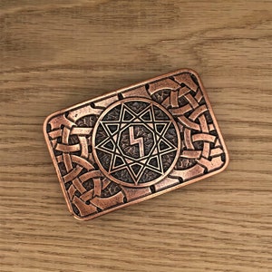 May include: A copper-colored belt buckle with an intricate design featuring a star with eight points and a lightning bolt symbol in the center.