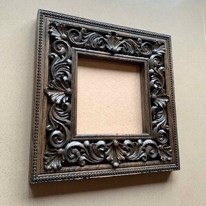 May include: A dark brown wooden picture frame with intricate carvings around the edges. The frame is empty and ready to display a photo or artwork.