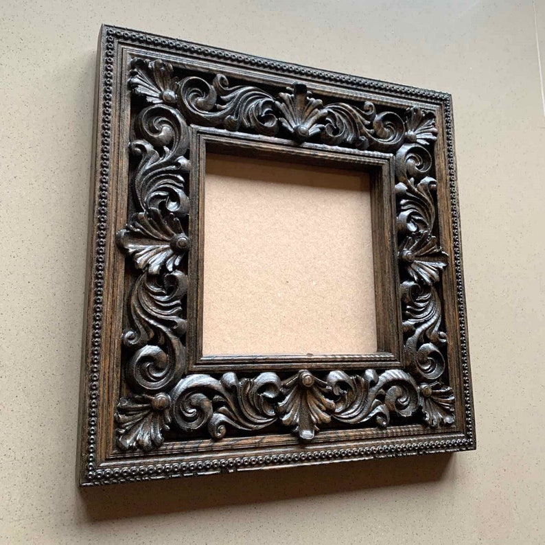 May include: A dark brown wooden picture frame with intricate carvings around the edges. The frame is empty and ready to display a photo or artwork.
