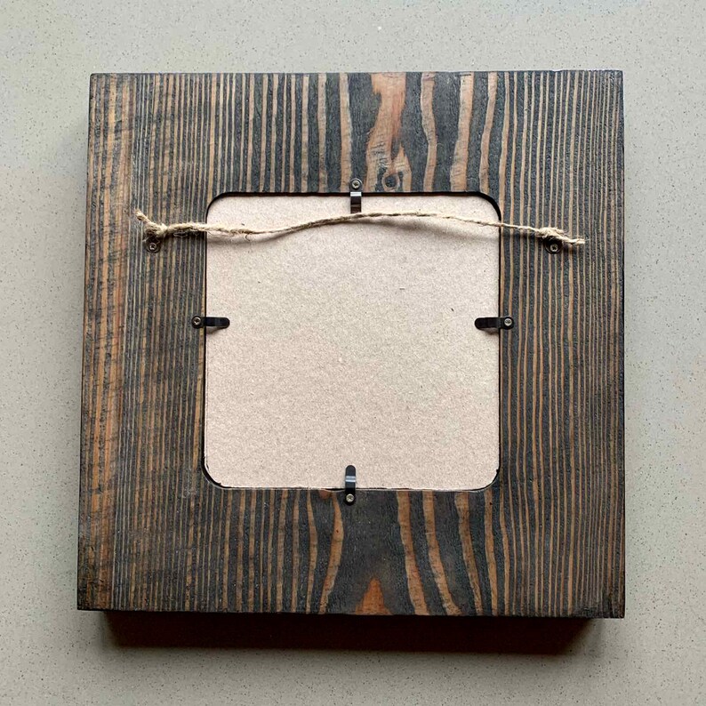 May include: A dark wood picture frame with a light brown mount and a piece of twine attached to the back for hanging.