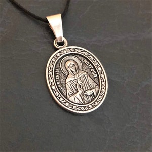 May include: Silver oval pendant with a religious image of a woman with a halo and the text "СВЯТАЯ МАТРОНА" in Cyrillic script.