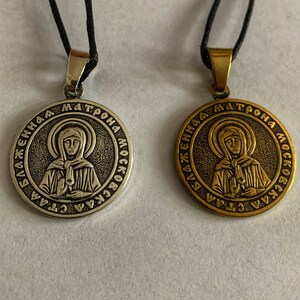 May include: Two silver and gold pendants with black cords. Both pendants feature a round image of a woman with a halo and the text "СВ. МАТРОНА МОСКОВСКАЯ" around the image.