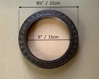 May include: A round, dark brown wooden frame with intricate carvings. The frame measures 8 1/4 inches in diameter and has an inner diameter of 6 inches.