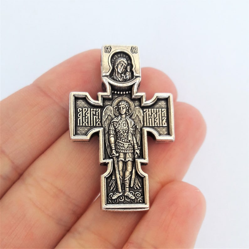 K&ouml;nnte beinhalten: Silberner orthodoxer Kreuzanh&auml;nger mit einem Bild des Erzengels Michael und der Jungfrau Maria. Das Kreuz ist mit komplizierten Details und kyrillischen Buchstaben verziert.