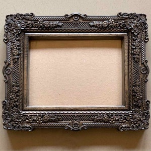 May include: A dark brown wooden picture frame with ornate carvings and a detailed floral design. The frame has a rectangular shape and a slightly raised edge.