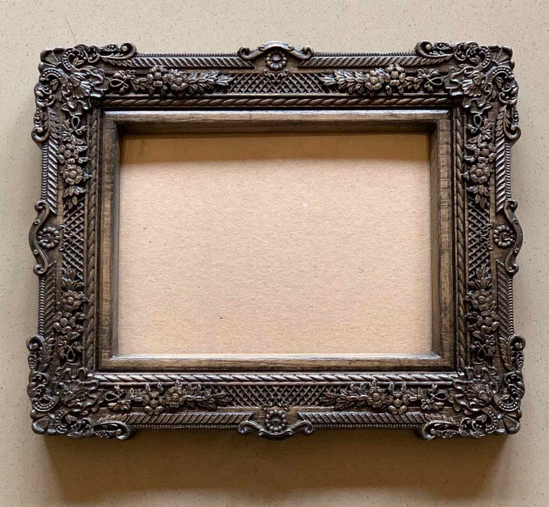 May include: A dark brown wooden picture frame with ornate carvings and a detailed floral design. The frame has a rectangular shape and a slightly raised edge.
